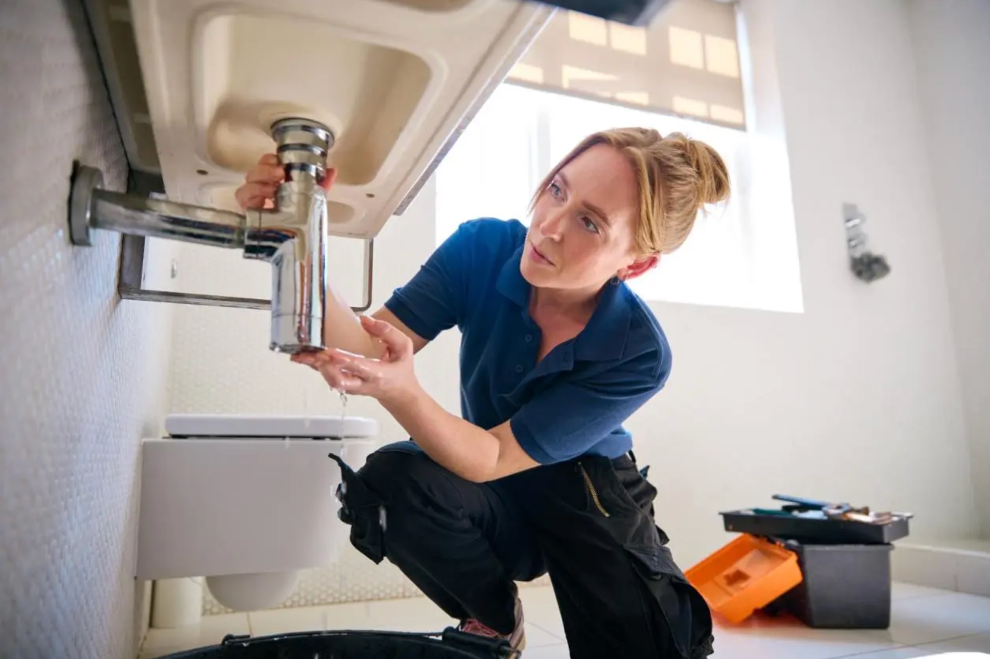 A plumber working under a sink while her phone is answered for her